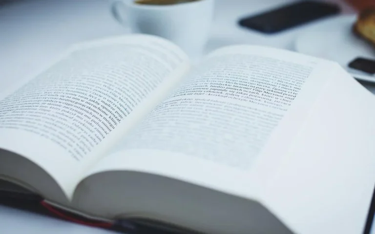 Libro abierto y una taza de café sobre la mesa de estudio